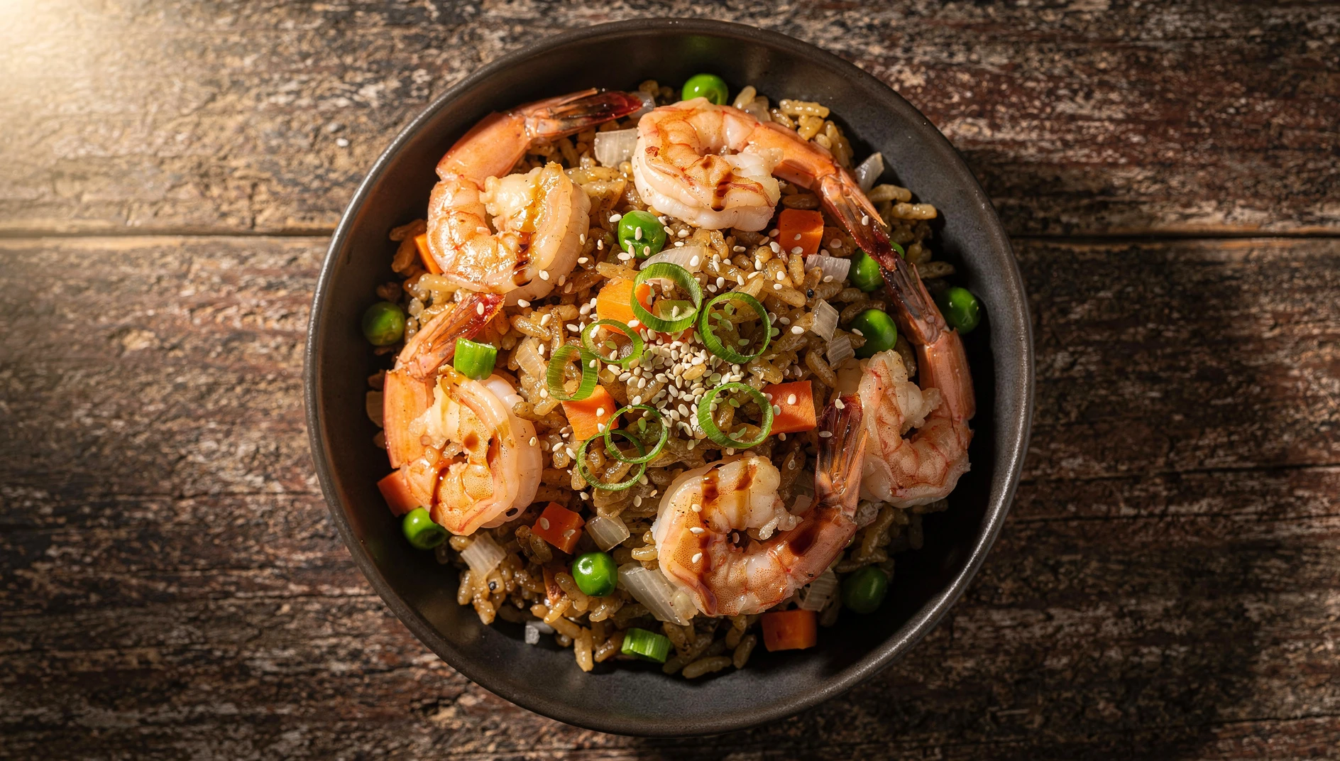 Arroz frito chino con camarones, guisantes y zanahoria servido en un bol de cerámica oscura