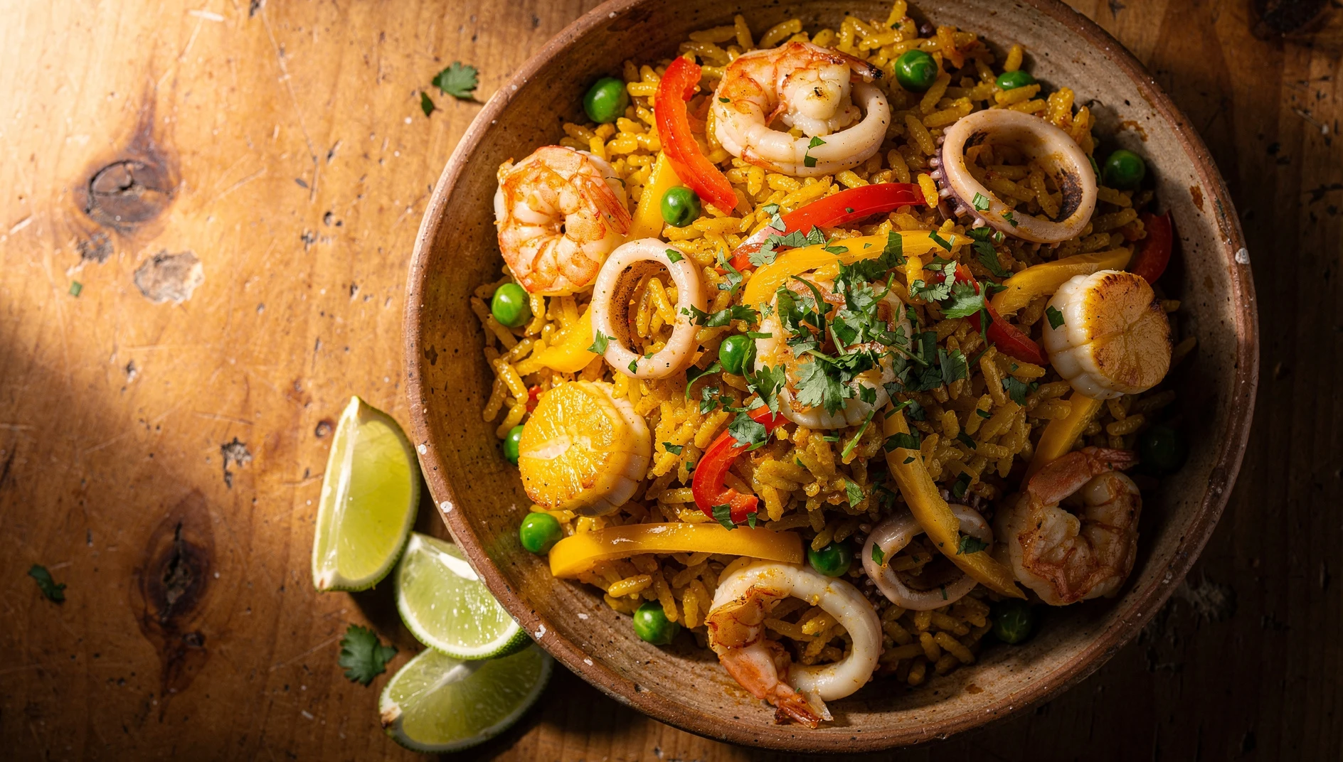 Arroz con mariscos peruano servido en un bol de barro con langostinos, calamares, conchas de abanico y cilantro fresco