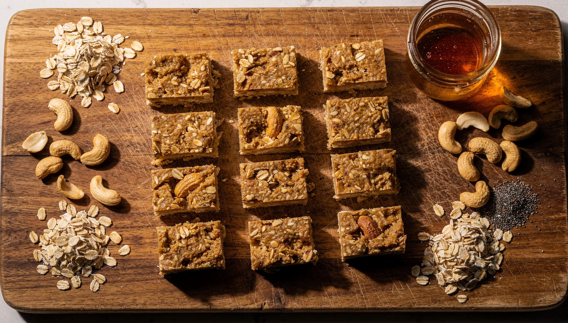Barritas energéticas veganas de avena y mantequilla de maní cortadas en porciones sobre una tabla de madera con ingredientes alrededor