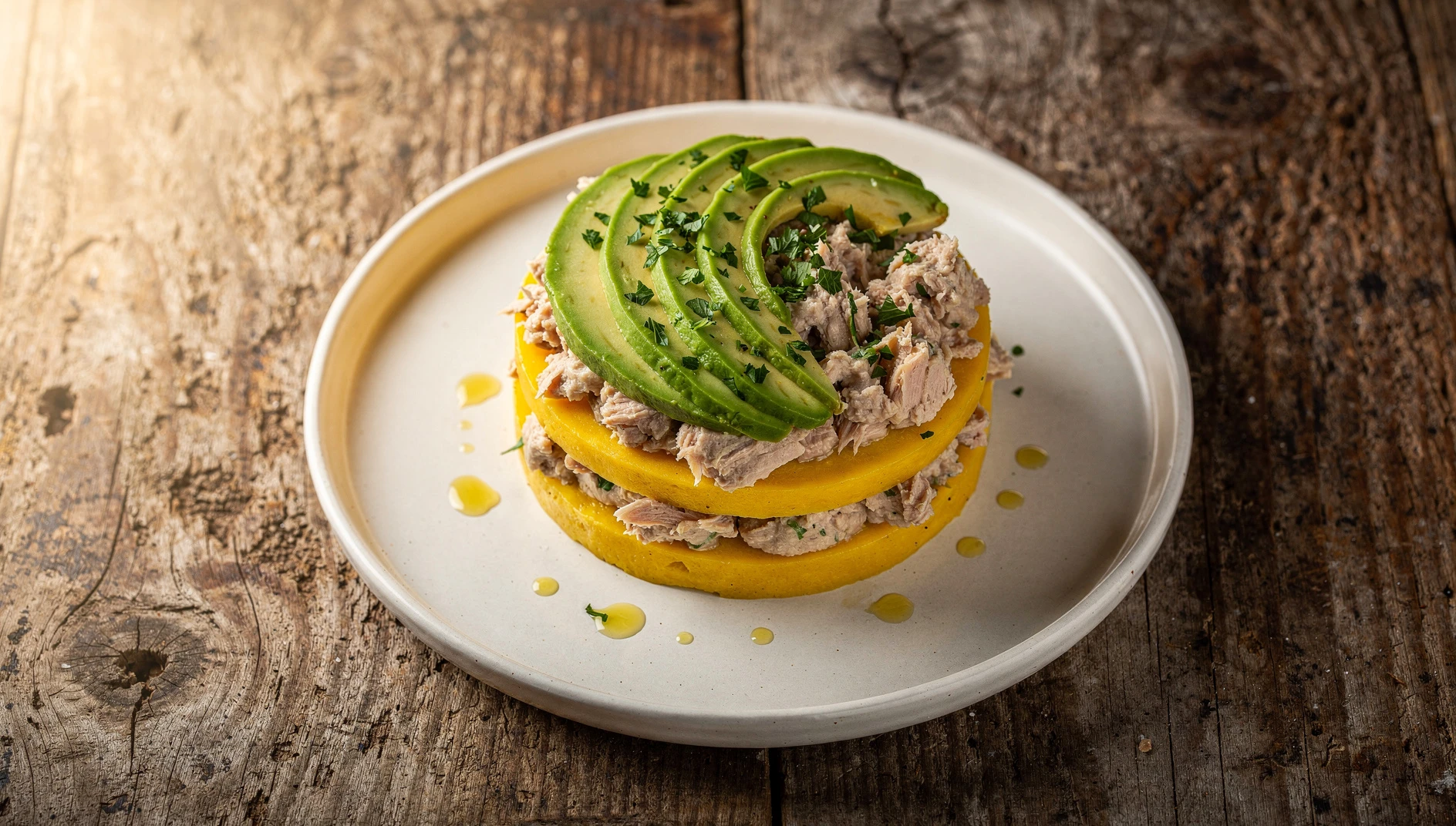 Causa limeña de atún con aguacate y perejil fresco servida en plato blanco