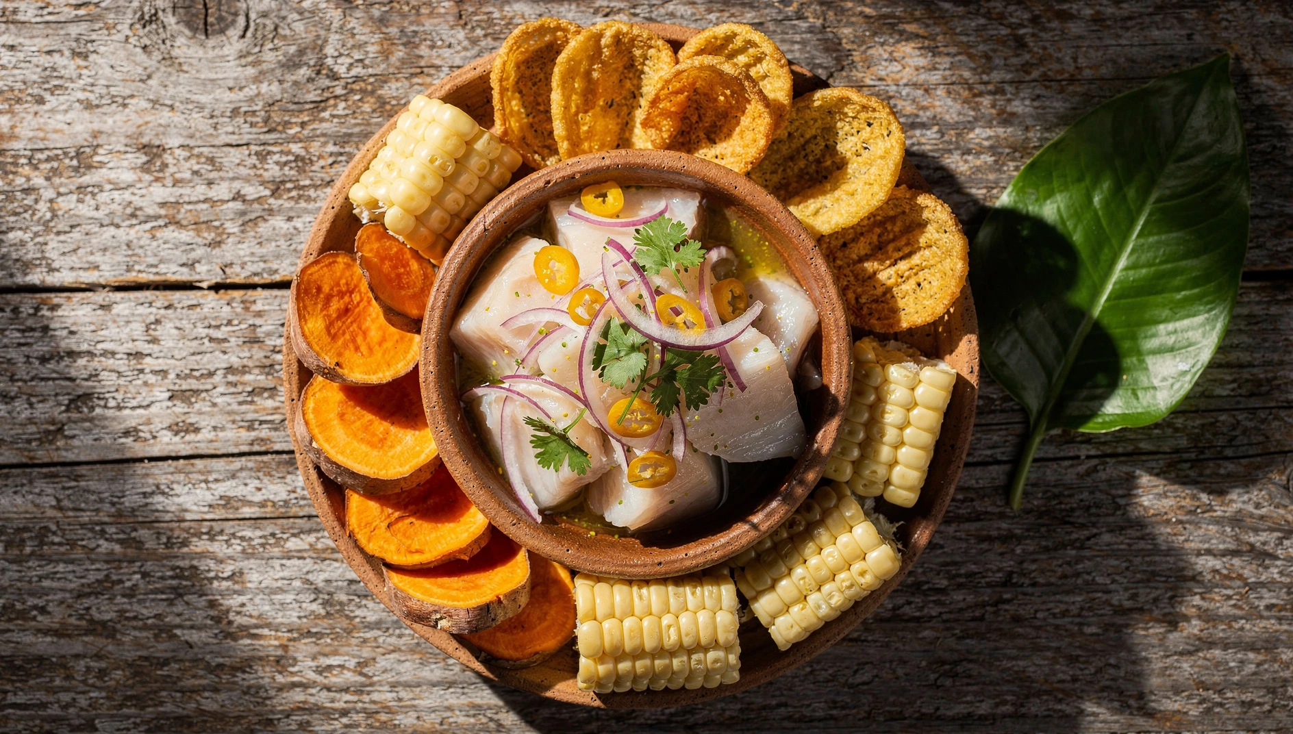 Ceviche amazónico de paiche en bol de barro con cebolla roja, ají charapita y cilantro, acompañado de chifles y camote