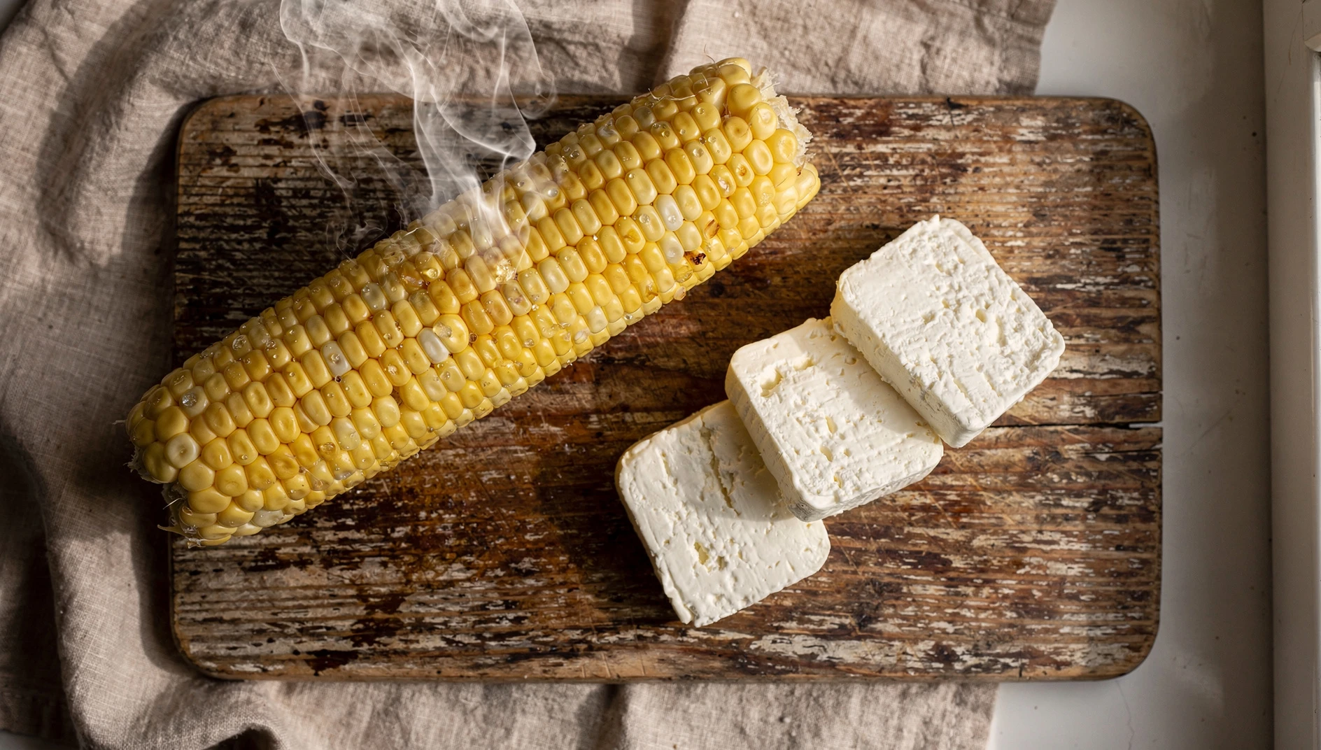 Choclo cocido con rodajas de queso serrano sobre tabla de madera rústica
