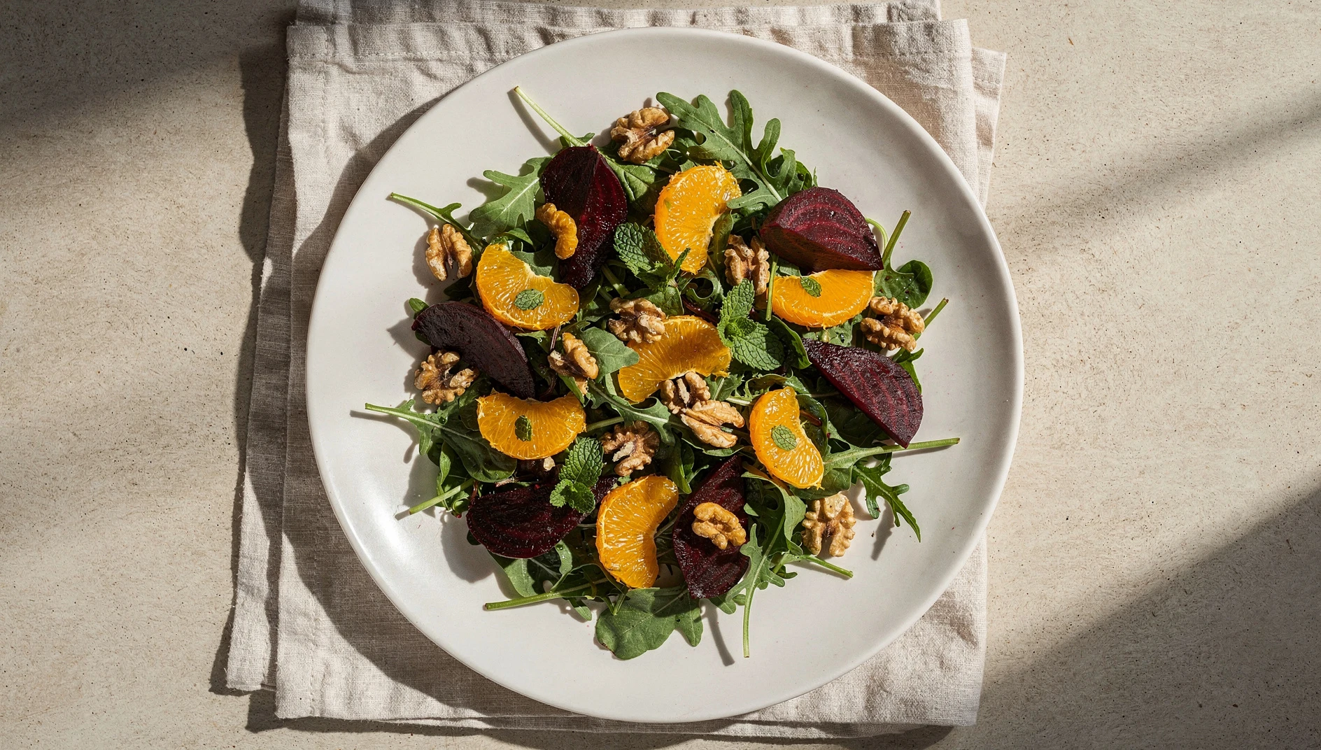 Ensalada vegana de beterraga asada con gajos de naranja, rúcula y nueces tostadas sobre plato de cerámica blanca