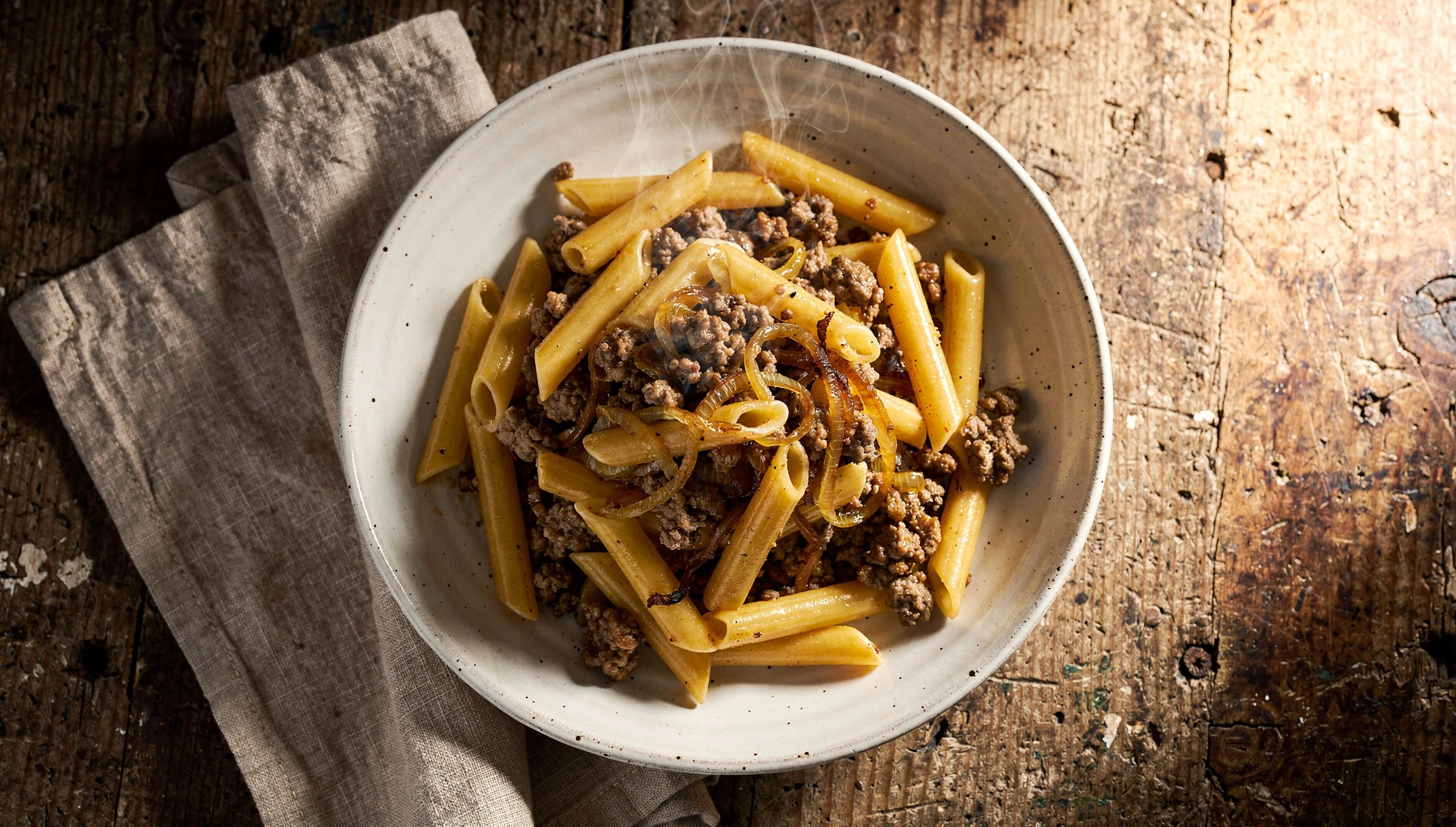 Plato de makarony po-flotski con pasta corta y carne picada dorada servido en bol de cerámica blanca