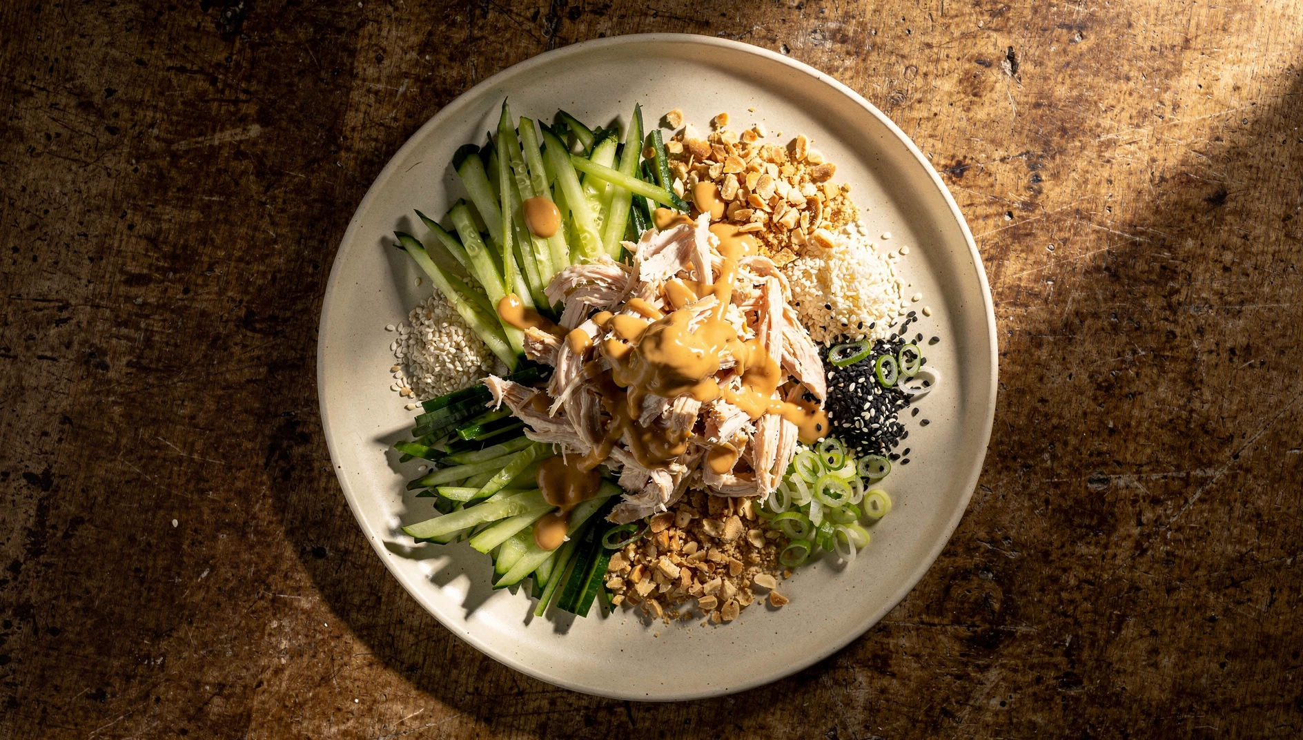 Ensalada fría de pollo bang bang con salsa de sésamo, pepino en juliana y cacahuetes tostados