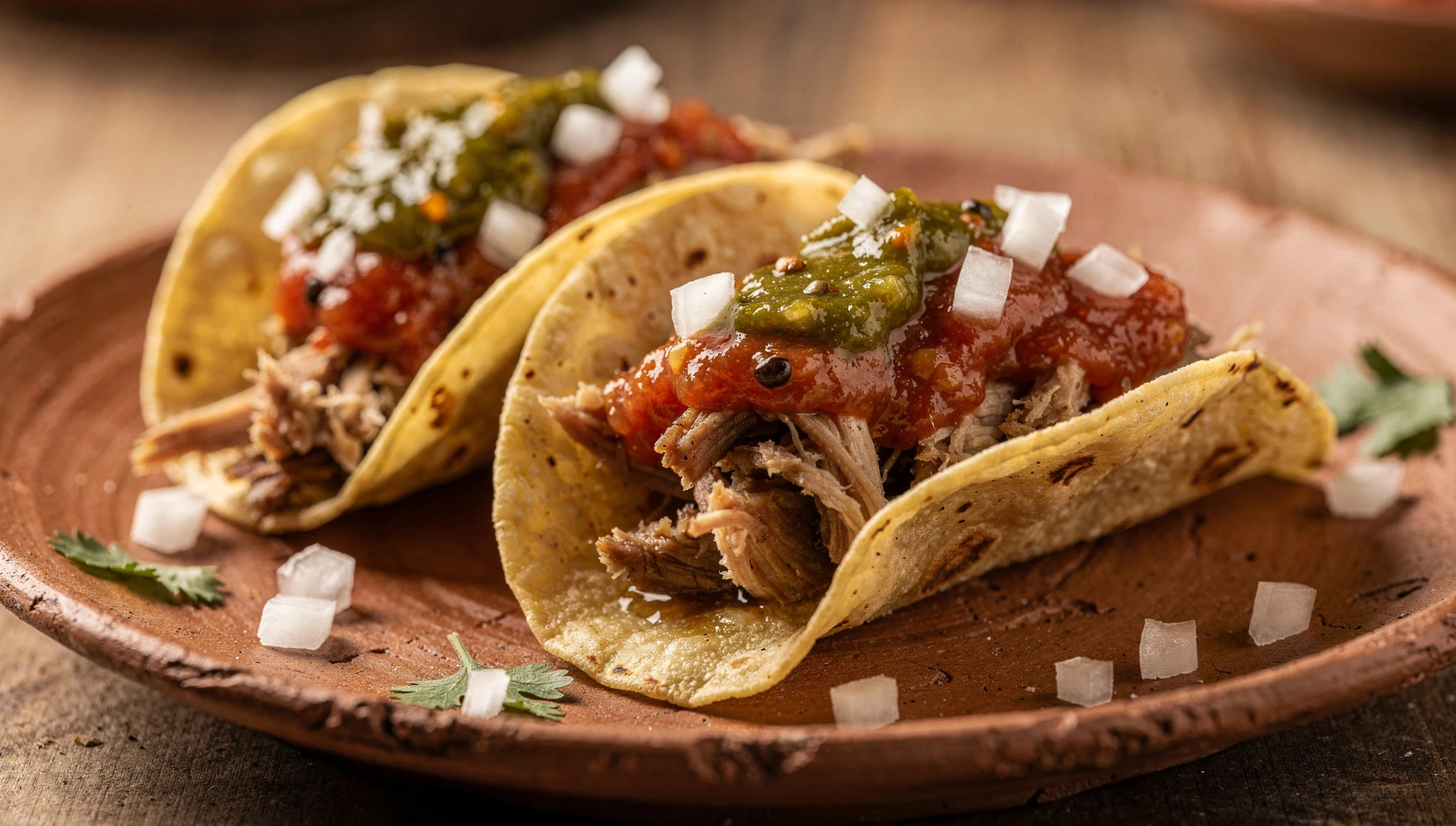 Chalupas poblanas con carne deshebrada, cebolla picada y salsa roja sobre plato de barro