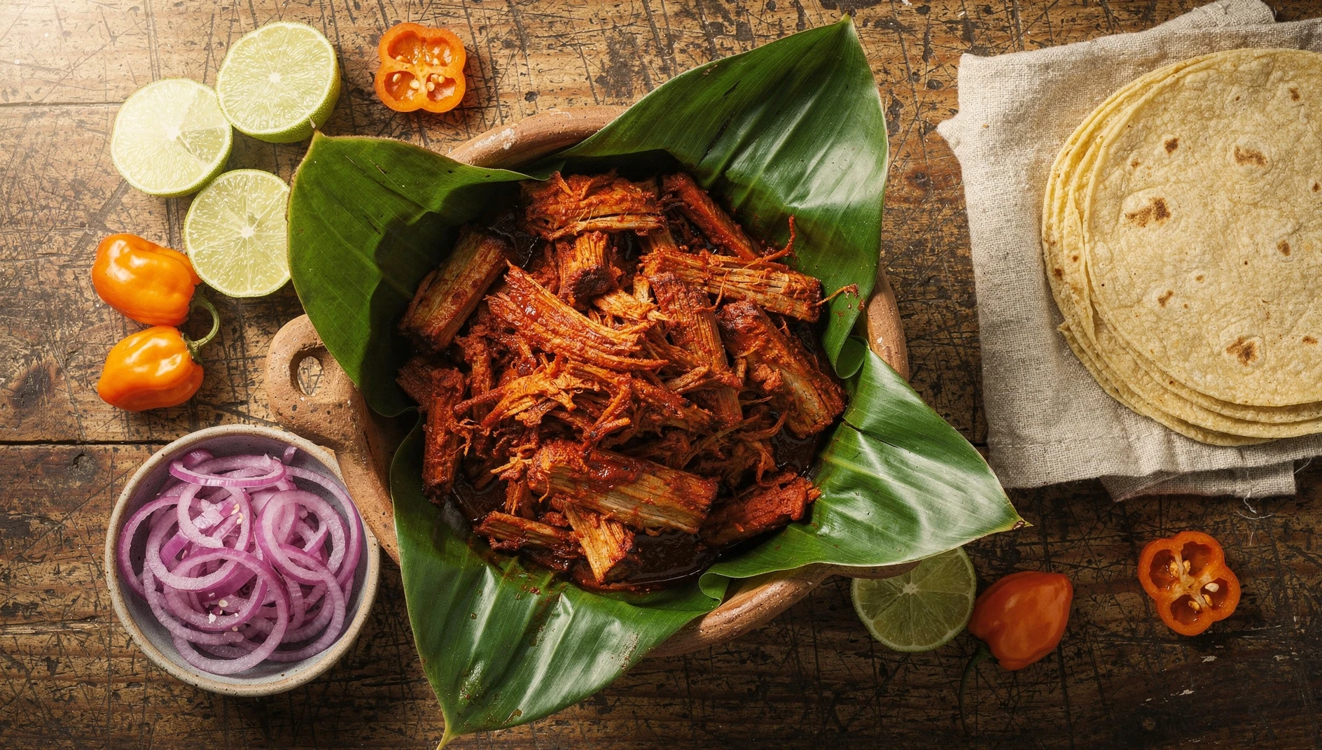 Cochinita pibil yucateca desmenuzada en cazuela de barro con cebolla morada encurtida y tortillas de maíz