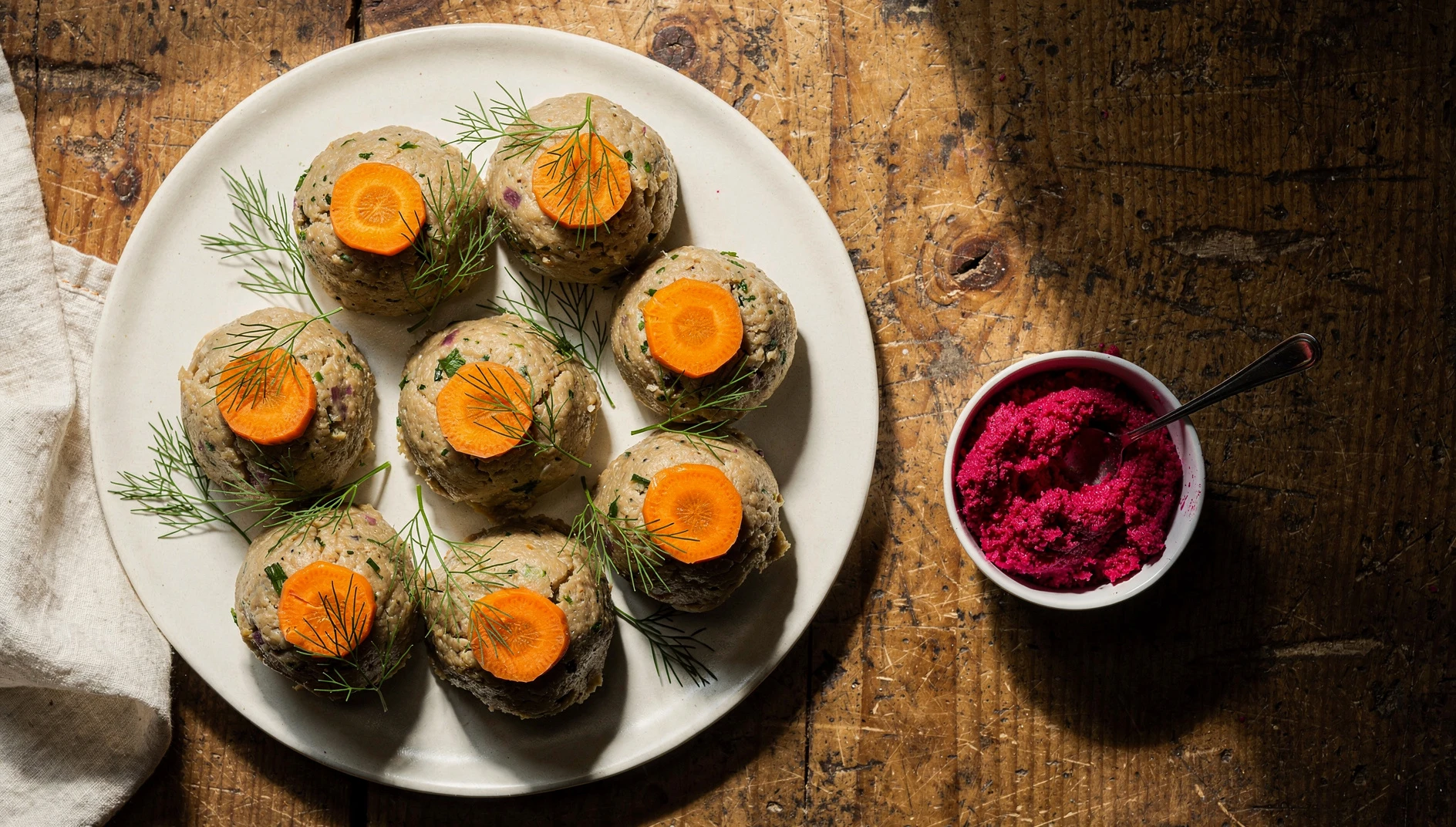 Quenelles de gefilte fish servidas en bandeja blanca con zanahorias cocidas y eneldo fresco