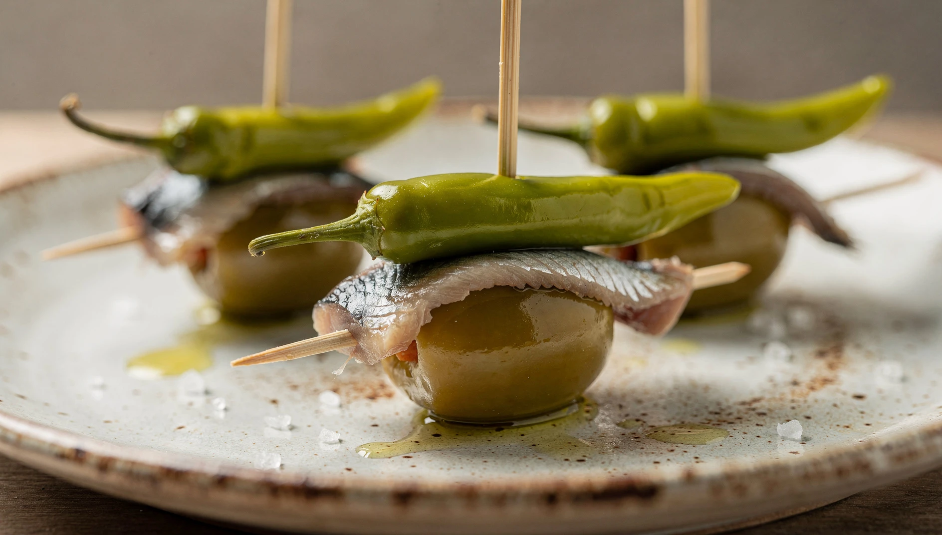 Tres gildas donostiarras con aceituna verde, anchoa enrollada y guindilla en vinagre sobre plato de cerámica blanca