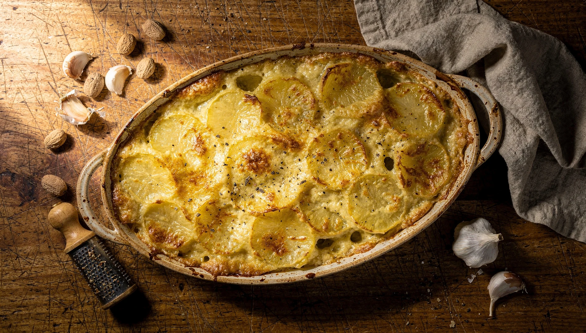 Fuente de gratin dauphinois recién sacada del horno con capas de papas a la crema doradas y burbujeantes