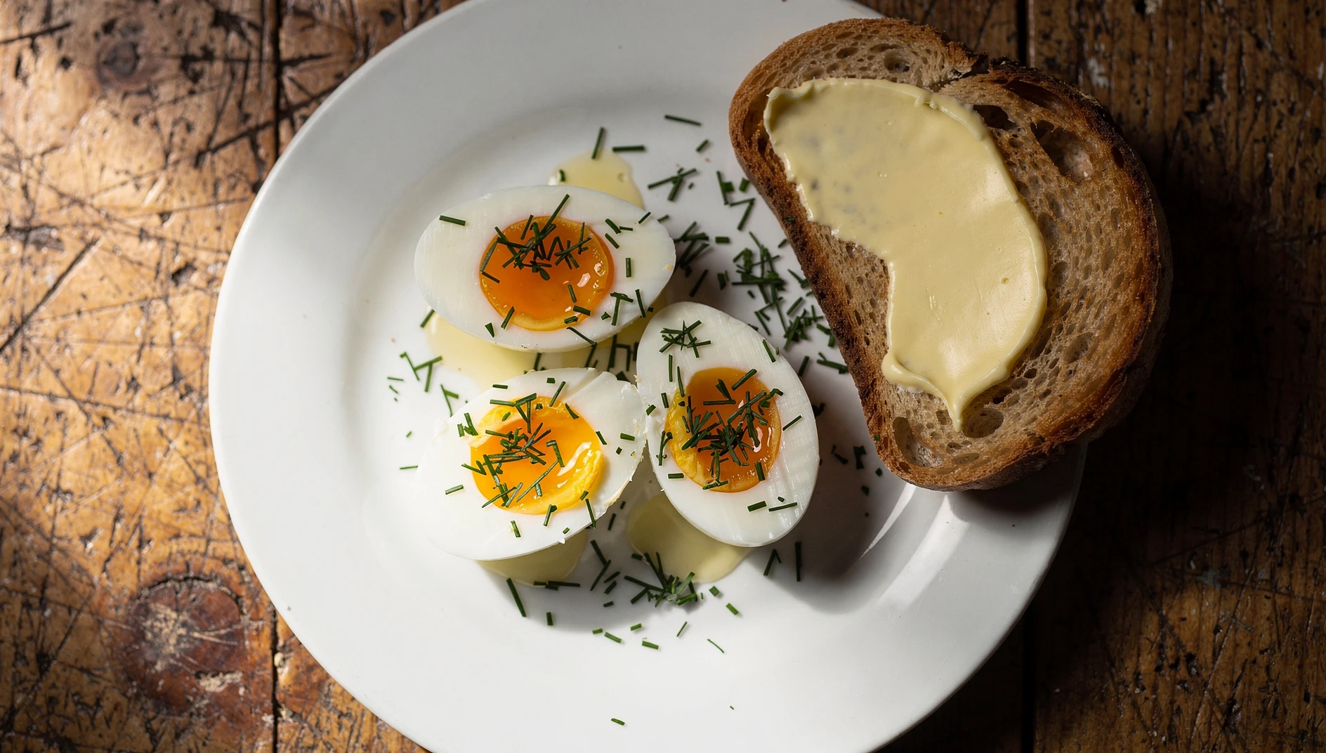 Huevos en camisita ucranianos pelados sobre plato blanco con eneldo fresco y pan tostado