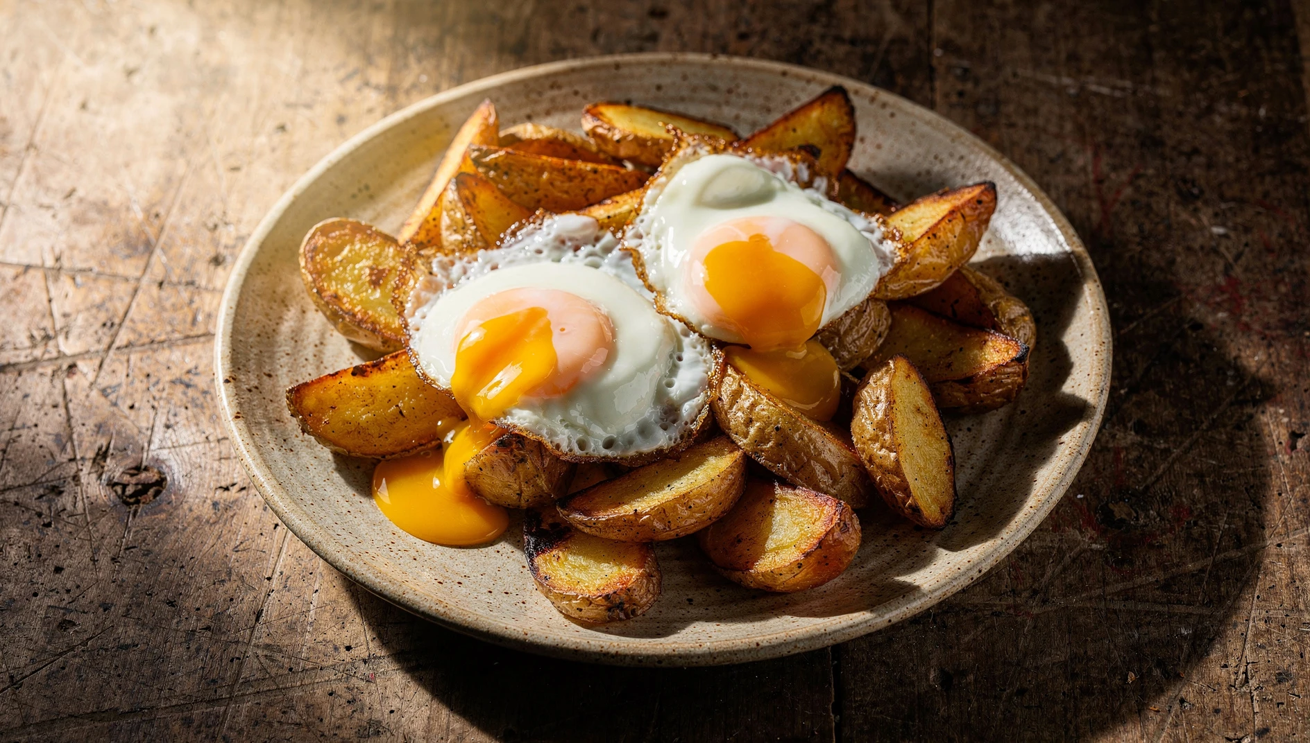 Plato de huevos rotos madrileños con patatas fritas doradas y yemas líquidas rotas encima