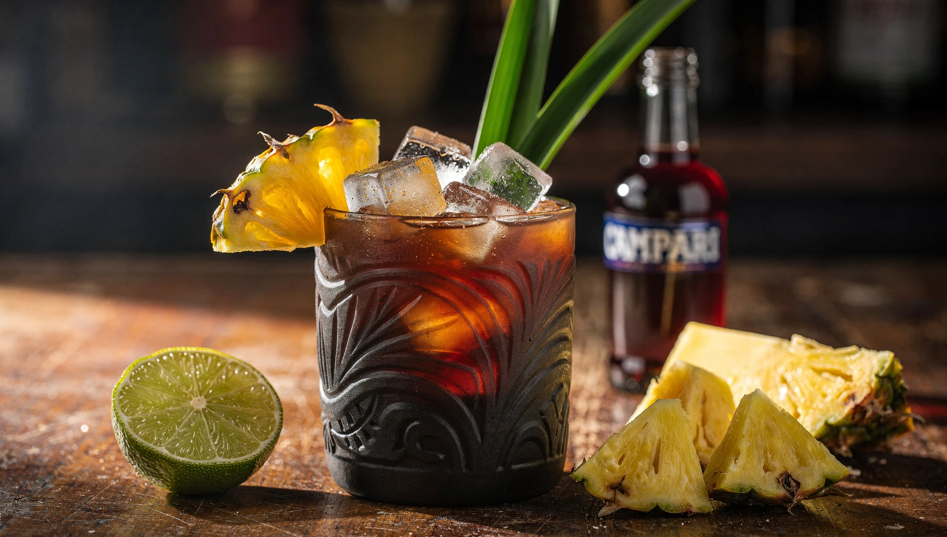 Cóctel Jungle Bird con ron oscuro, Campari y zumo de piña servido en vaso tiki con hielo y decoración de piña fresca