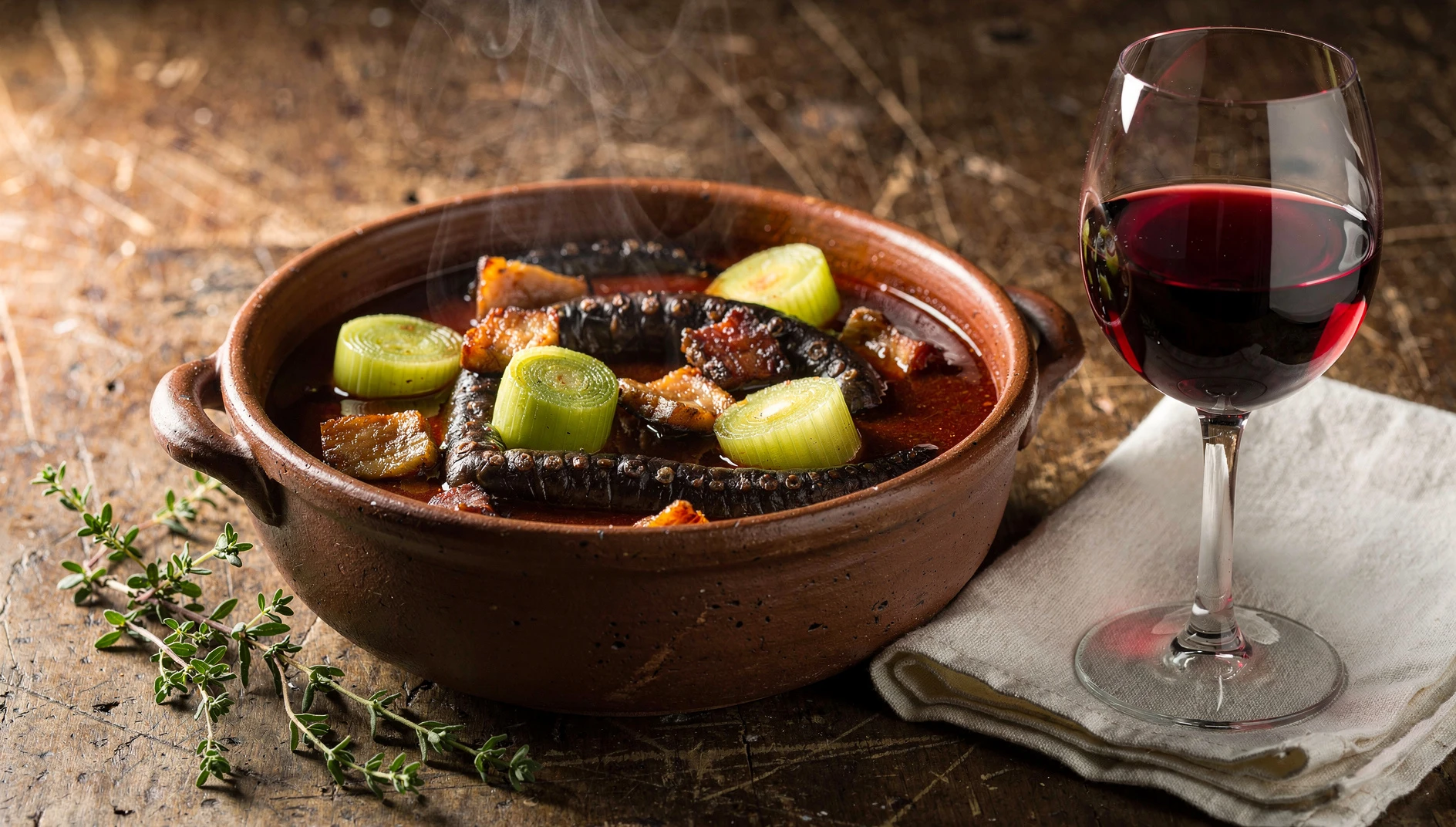 Cazuela de lamproie à la bordelaise con salsa de vino tinto, puerros y tocino servida en mesa de madera rústica