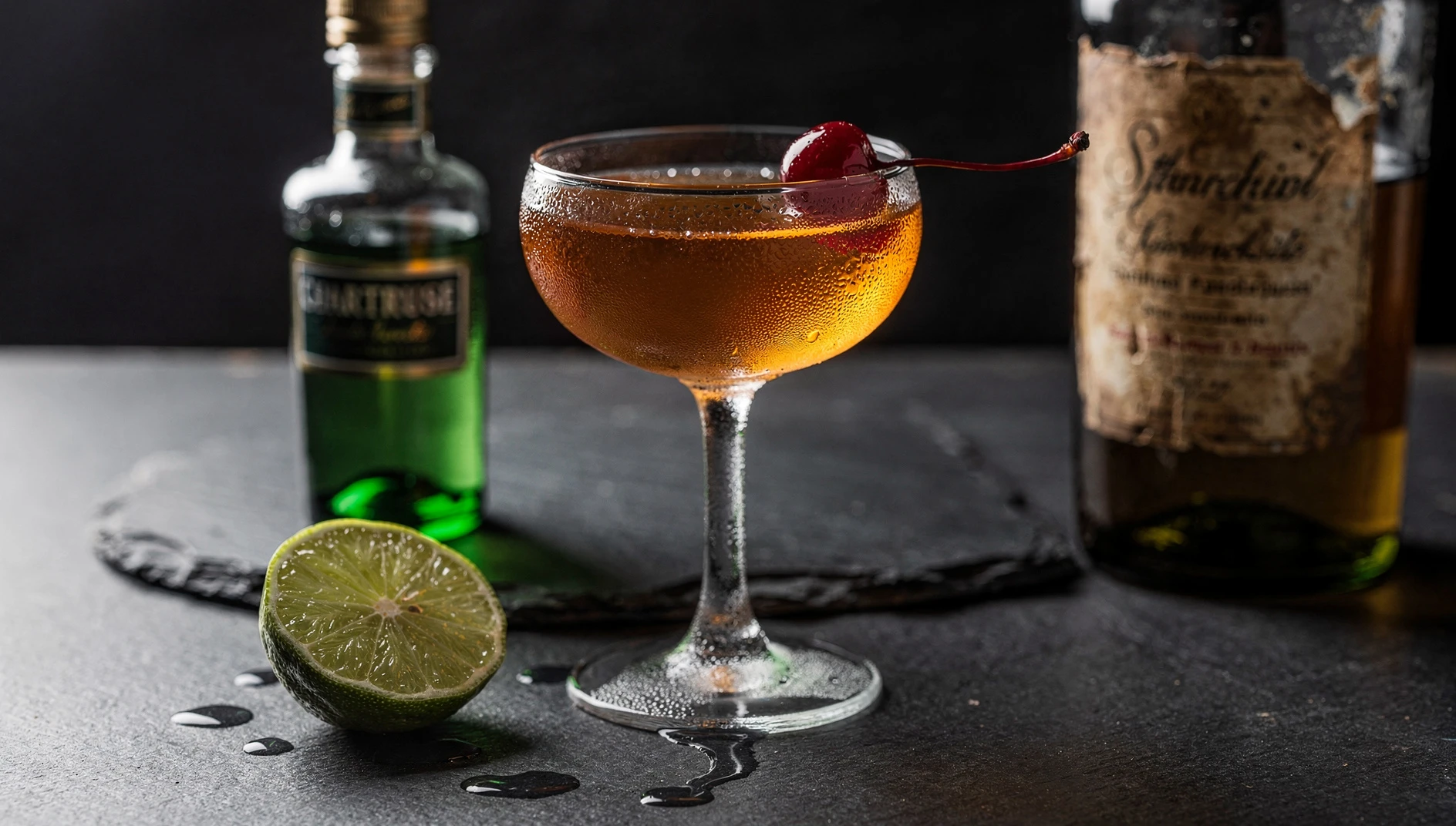 Copa coupette con el cóctel Last Word, acompañada de lima, Chartreuse verde y una cereza marrasquino
