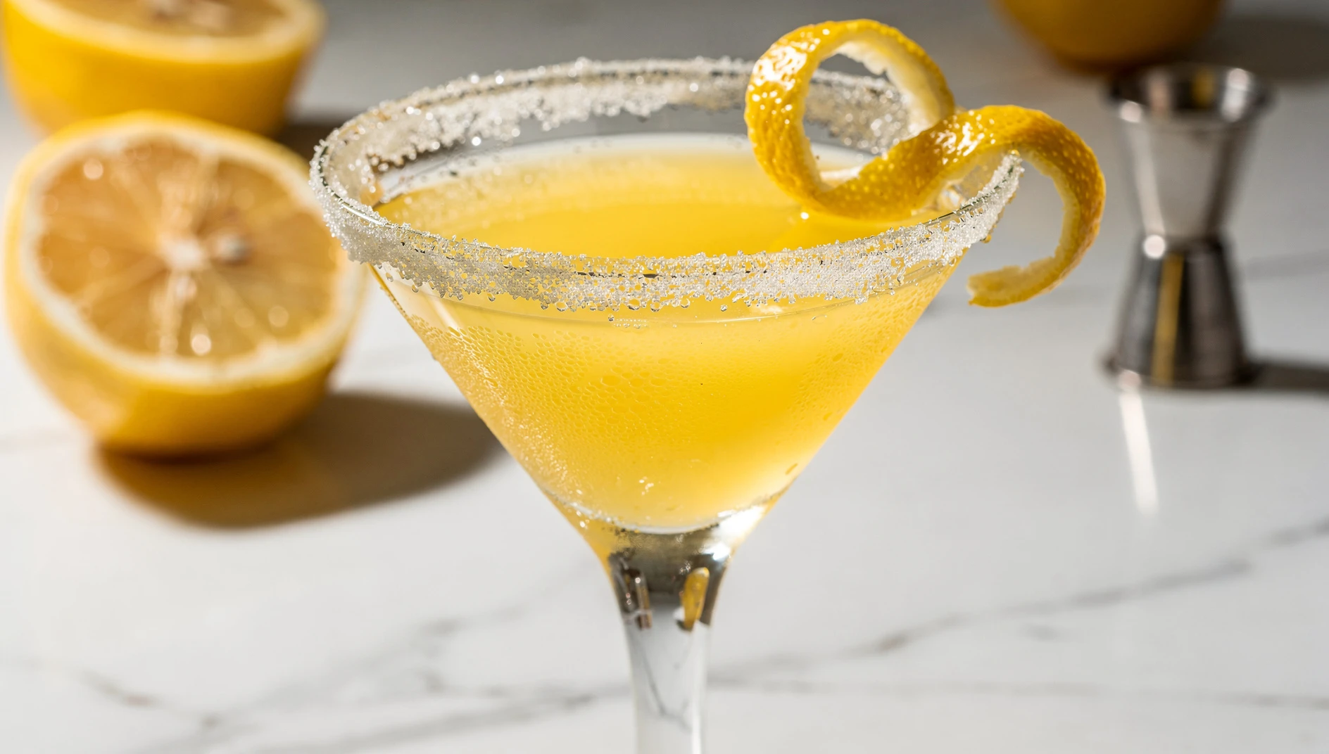Copa de martini con borde de azúcar y lemon drop martini de color amarillo pálido, decorada con una espiral de limón