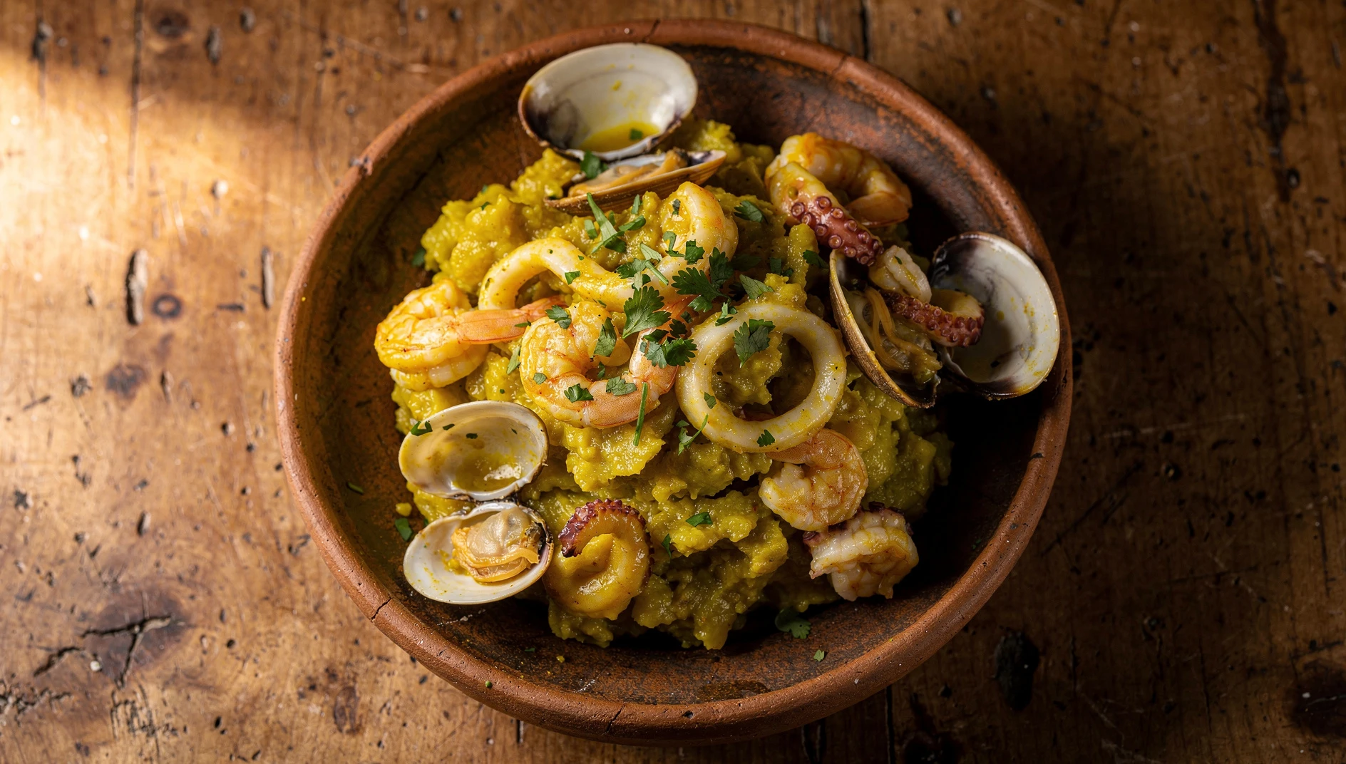 Plato de majarisco tumbesino con mariscos frescos y plátano verde majado servido en bol de barro