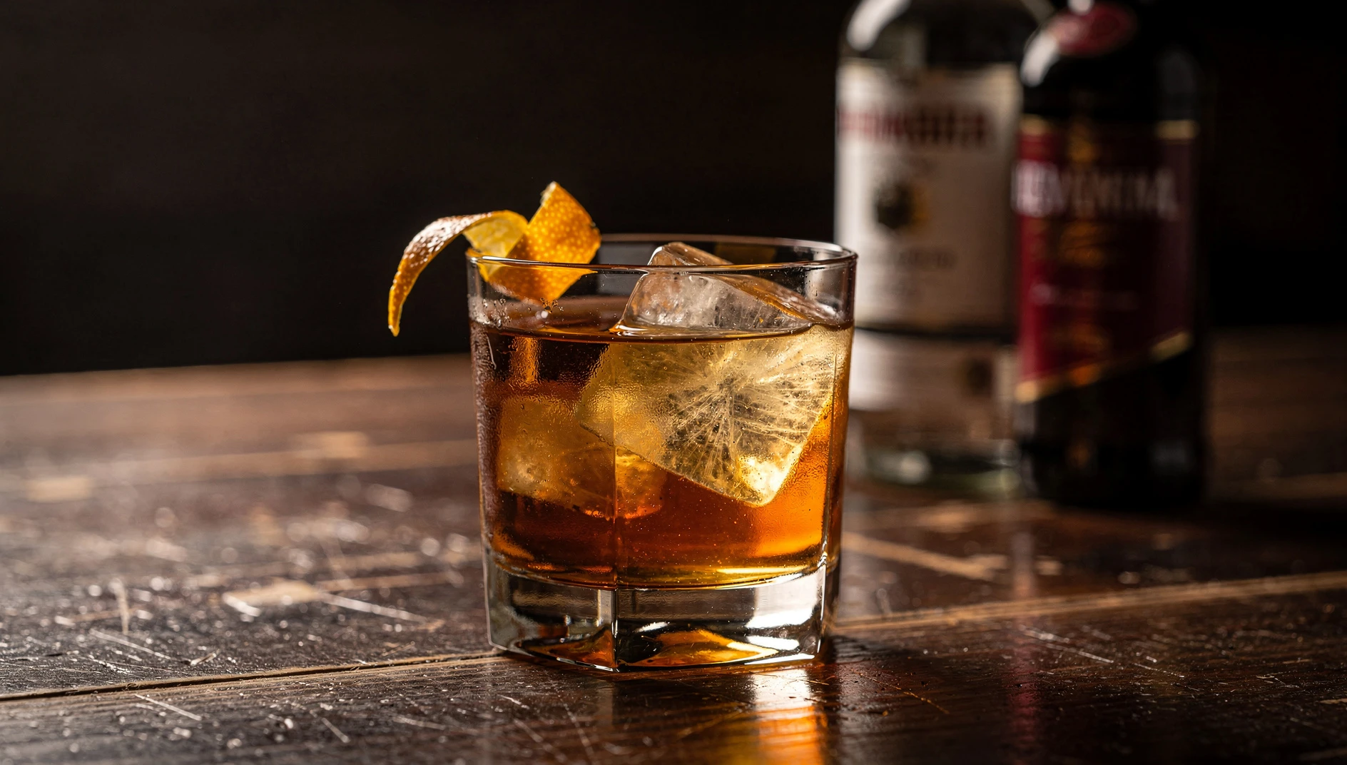 Rabo de Galo servido en vaso old fashioned con hielo y twist de naranja sobre una barra de madera oscura