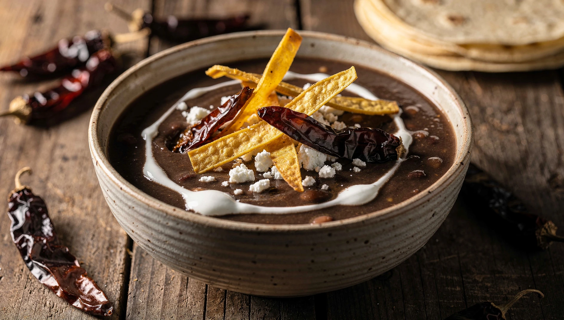 Tazón de sopa tarasca con tiras de tortilla frita, crema y queso Cotija sobre mesa rústica de madera