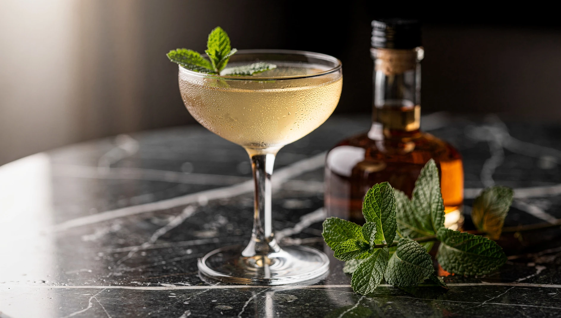 Copa coupe con el cóctel Stinger preparado con brandy y licor de menta blanca, decorado con hoja de menta fresca