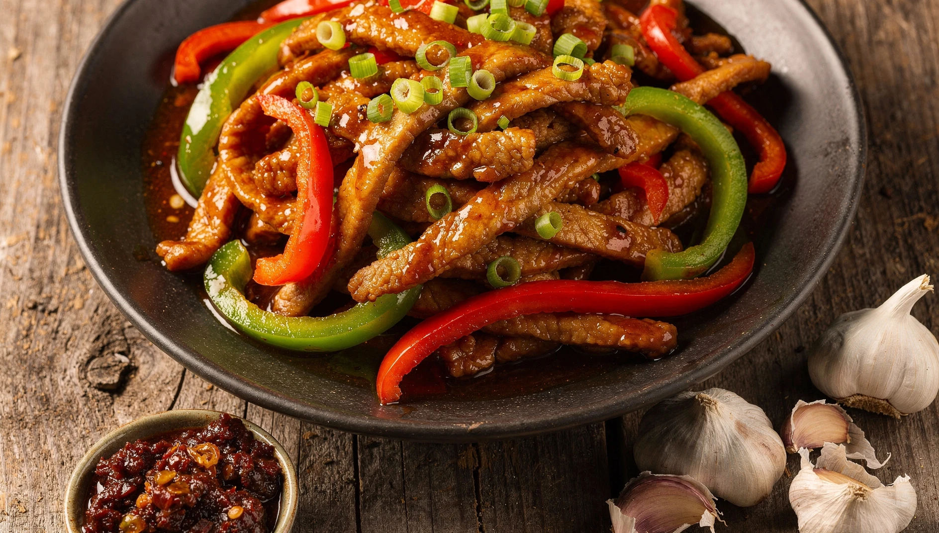Plato de yu xiang rousi con tiras de cerdo en salsa yuxiang, pimientos y cebolleta sobre bol de cerámica oscura