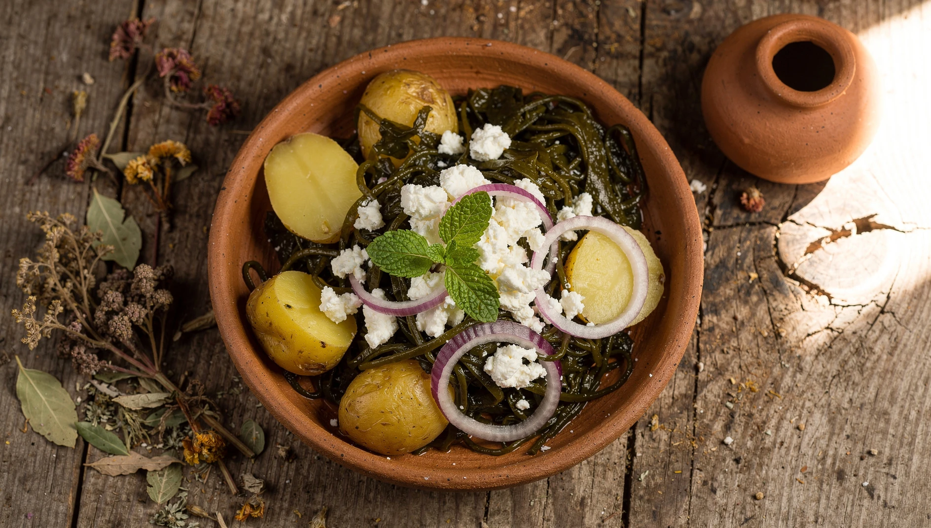 Plato de yuyo passi de Junín servido en bol de barro con papas, queso fresco y hierbabuena sobre mesa de madera rústica
