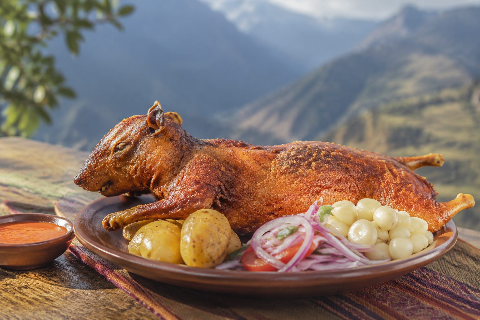 Cuy peruano servido con papas y salsa de ají en una mesa andina